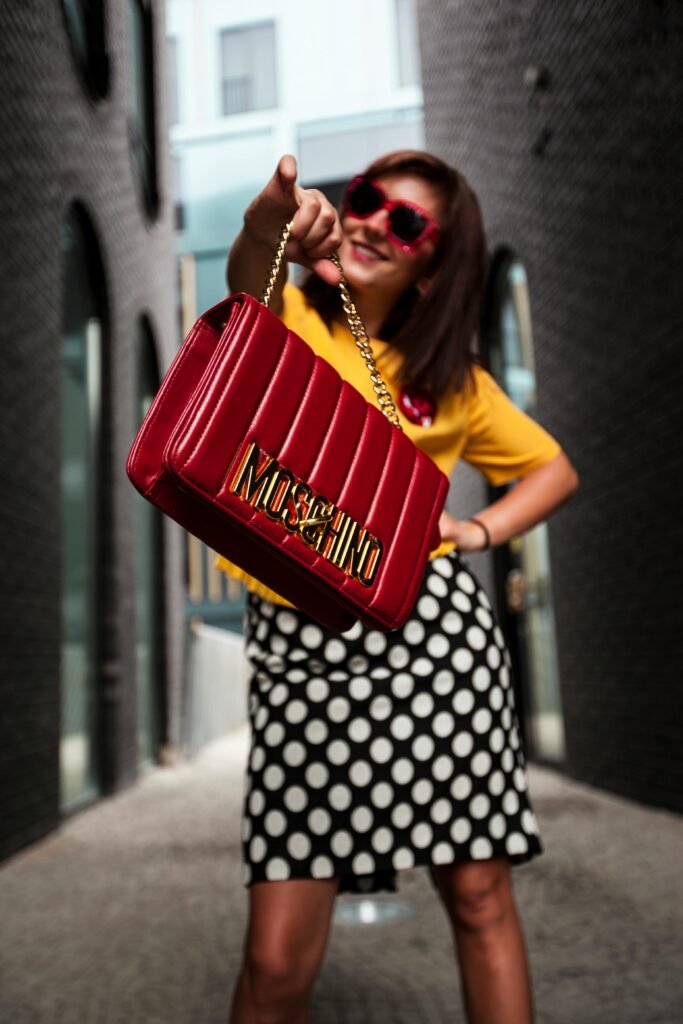 Fashionable woman in sunglasses flaunting a Moschino bag on a city street.